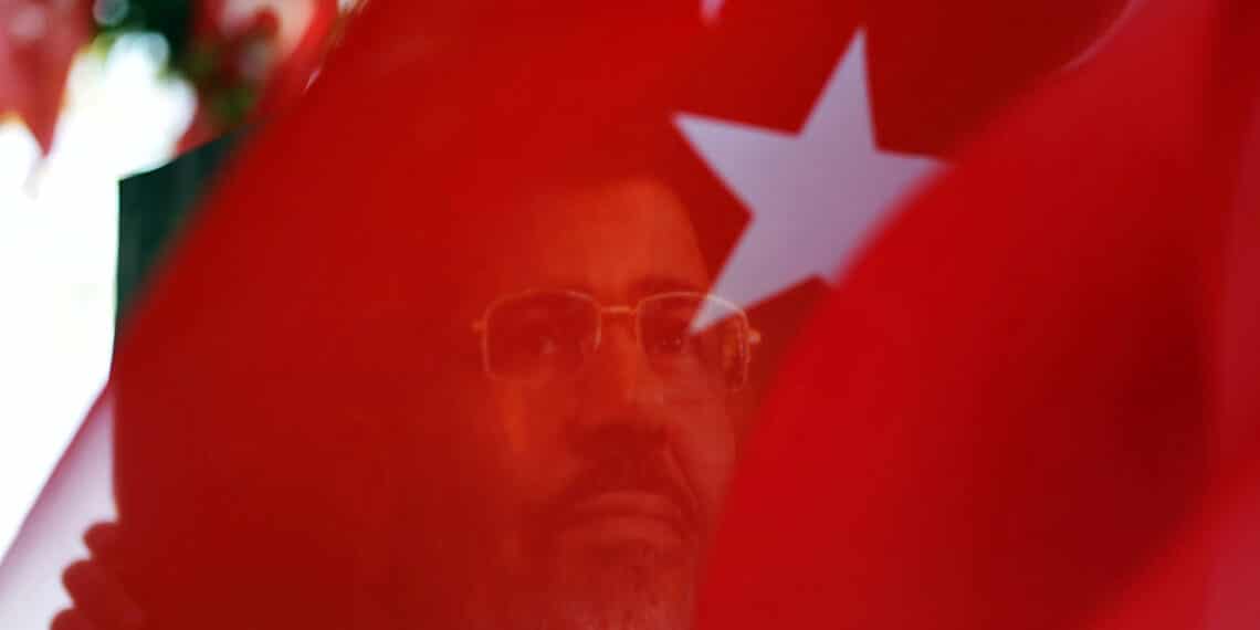 A portait of ousted Egyptian president Mohamed Morsi is seen through a Turkish flag during a rally on August 25, 2013 in Istanbul to support ousted Egyptian president Morsi and protest against killings in Syria and Egypt. The "Rabia sign" has become a symbol to remember the massacre in Egypt at the Rabaa al-Adawiya Square where the anti-coup protests took place.          AFP PHOTO / BULENT KILIC        (Photo credit should read BULENT KILIC/AFP via Getty Images)