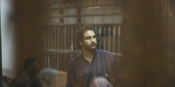 CAIRO, EGYPT - MAY 23: Egyptian activist Alaa Abdel Fattah stands inside a defendant's cage during  his new trial in Cairo, Egypt on May 23, 2015 with 24 other defendants including former Egyptian President Mohammad Morsi on trial for insulting the judiciary. Cairo Criminal court postponed on Saturday, the trial of former President, Morsi, to July 27. (Photo by Mostafa el-Shemy/Anadolu Agency/Getty Images)