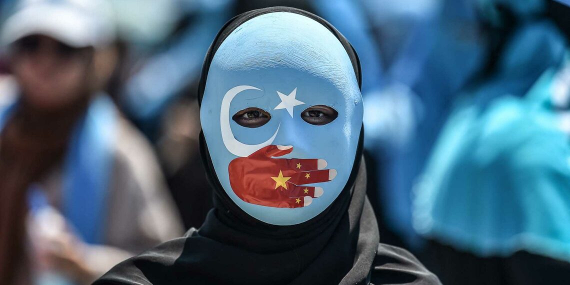 TOPSHOT - A demonstrator wearing a mask painted with the colours of the flag of East Turkestan and a hand bearing the colours of the Chinese flag attends a protest of supporters of the mostly Muslim Uighur minority and Turkish nationalists to denounce China's treatment of ethnic Uighur Muslims during a deadly riot in July 2009 in Urumqi, in front of the Chinese consulate in Istanbul, on July 5, 2018. - Nearly 200 people died during a series of violent riots that broke out on July 5, 2009 over several days in Urumqi, the capital city of the Xinjiang Uyghur Autonomous Region, in northwestern China, between Uyghurs and Han people. (Photo by OZAN KOSE / AFP) (Photo by OZAN KOSE/AFP via Getty Images)