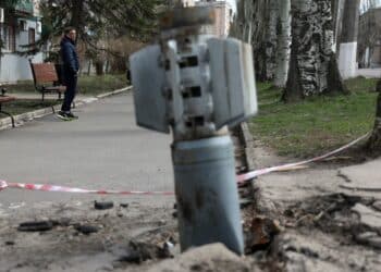 A man walks past an unexploded tail section of a 300mm rocket which appear to contained cluster bombs launched from a BM-30 Smerch multiple rocket launcher embedded in the ground after shelling in Lysychansk, Lugansk region on April 11, 2022. (Photo by Anatolii STEPANOV / AFP)
