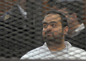 Egyptian prominent activicts Mohamed Adel stands in the accused dock during his trial on December 22, 2013, in Cairo. An Egyptian court sentenced three activists, Mohamed Adel, Ahmed Maher (unseen), the founder of the April 6 youth movement that led the revolt against former president Hosni Mubarak, and Ahmed Douma (unseen), all accused of spearheading the 2011 uprising against Mubarak to three years in jail for organising an unlicensed protest, judicial sources said. It was the first such verdict against non-Islamist protesters since the overthrow of president Mohamed Morsi in July, and was seen by rights groups as part of a widening crackdown on demonstrations by military-installed authorities. AFP PHOTO/STR        (Photo credit should read STRINGER/AFP via Getty Images)