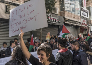 A Palestinian woman lifts a placard bearing verses by Palestinian poet Refaat Alareer who was reported killed in Gaza on December 7, as protesters carry a list of Gaza victims during a rally amid a general strike in Ramallah city in the occupied West Bank on December 11, 2023, in solidarity with Gaza as battles continue between Israel and the Palestinian militant group Hamas. (Photo by MARCO LONGARI / AFP)