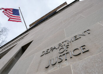WASHINGTON, DC - JANUARY 30: The US Flag flies above a sign marking the US Department of Justice (DOJ) headquarters building on January 20, 2024, in Washington, DC. (Photo by J. David Ake/Getty Images)