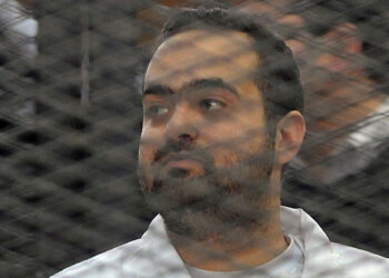 Egyptian prominent activicts Mohamed Adel stands in the accused dock during his trial on December 22, 2013, in Cairo. An Egyptian court sentenced three activists, Mohamed Adel, Ahmed Maher (unseen), the founder of the April 6 youth movement that led the revolt against former president Hosni Mubarak, and Ahmed Douma (unseen), all accused of spearheading the 2011 uprising against Mubarak to three years in jail for organising an unlicensed protest, judicial sources said. It was the first such verdict against non-Islamist protesters since the overthrow of president Mohamed Morsi in July, and was seen by rights groups as part of a widening crackdown on demonstrations by military-installed authorities. AFP PHOTO/STR