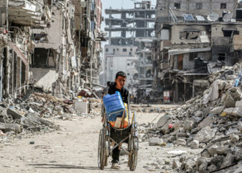 A boy pushes a wheelchair carrying water containers past the rubble of destroyed buildings along a street in Khan Yunis in the southern Gaza Strip on July 8, 2024 amid the ongoing conflict in the Palestinian territory between Israel and Hamas. (Photo by Bashar TALEB / AFP)