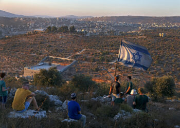 TOPSHOT - Israeli settler youths lift an Israeli flag in the newly-established wildcat outpost of Eviatar near the northern Palestinian city of Nablus in the occupied West Bank, on June 28, 2021, across from the Palestinian village of Beita. Jewish settlers agreed to leave a new outpost in the occupied West Bank that has stirred weeks of Palestinian protests following a deal with Israel's government, in an agreement confirmed by the interior ministry and settler leaders, under which they will leave the Eviatar outpost within days but their mobile homes will remain and Israeli troops will establish a base in the area. (Photo by MENAHEM KAHANA / AFP) (Photo by MENAHEM KAHANA/AFP via Getty Images)