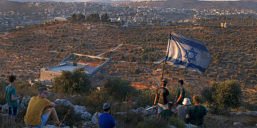 TOPSHOT - Israeli settler youths lift an Israeli flag in the newly-established wildcat outpost of Eviatar near the northern Palestinian city of Nablus in the occupied West Bank, on June 28, 2021, across from the Palestinian village of Beita. Jewish settlers agreed to leave a new outpost in the occupied West Bank that has stirred weeks of Palestinian protests following a deal with Israel's government, in an agreement confirmed by the interior ministry and settler leaders, under which they will leave the Eviatar outpost within days but their mobile homes will remain and Israeli troops will establish a base in the area. (Photo by MENAHEM KAHANA / AFP) (Photo by MENAHEM KAHANA/AFP via Getty Images)