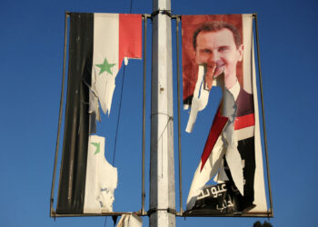 A billboard bearing a picture of Syria's President Bashar al-Assad and a national flag are torn by anti-government fighters in the northern city of Aleppo on November 30, 2024. Jihadists and their Turkish-backed allies breached Syria's second city of Aleppo on November 29, as they pressed a lightning offensive against forces of the Iranian- and Russian-backed government. (Photo by Omar HAJ KADOUR / AFP)