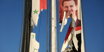 A billboard bearing a picture of Syria's President Bashar al-Assad and a national flag are torn by anti-government fighters in the northern city of Aleppo on November 30, 2024. Jihadists and their Turkish-backed allies breached Syria's second city of Aleppo on November 29, as they pressed a lightning offensive against forces of the Iranian- and Russian-backed government. (Photo by Omar HAJ KADOUR / AFP)