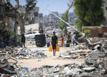 A Palestinian man carries two water containers past destroyed buildings in Khan Yunis, in the southern Gaza Strip on June 11, 2024, amid the ongoing conflict between Israel and the Palestinian Hamas militant group. (Photo by Eyad BABA / AFP)