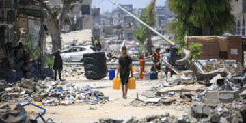 A Palestinian man carries two water containers past destroyed buildings in Khan Yunis, in the southern Gaza Strip on June 11, 2024, amid the ongoing conflict between Israel and the Palestinian Hamas militant group. (Photo by Eyad BABA / AFP)