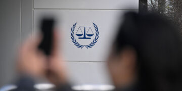 A bystander takes an image of the logo outside the exterior of the International Criminal Court (ICC) in The Hague on March 28, 2026. (Photo by JOHN THYS / AFP via Getty Images)